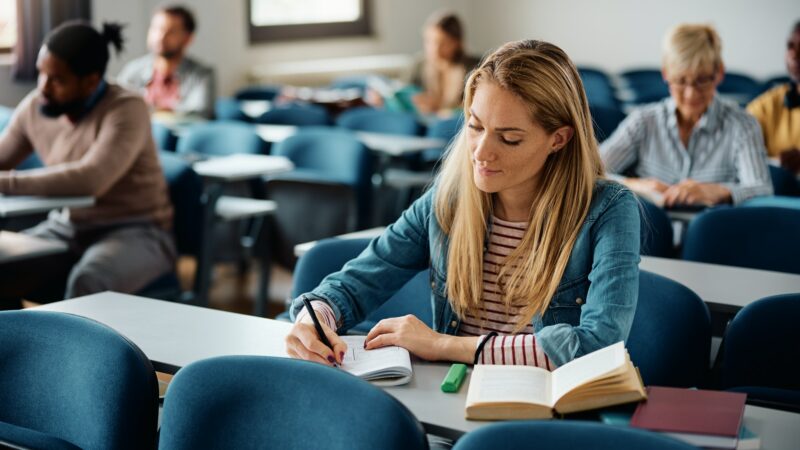 Mid adult woman writing in notebook while attending a class at the university