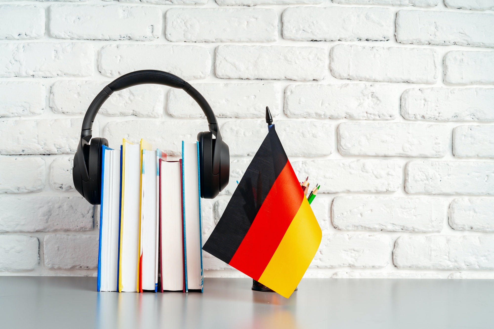 Stack of books and flag of Germany on desk. German language learning concept